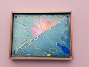 Hilma Klint Art: the pale blue painting with the pink flower and "H.a.K." initials, and the grid of nine brown-paper drawings.