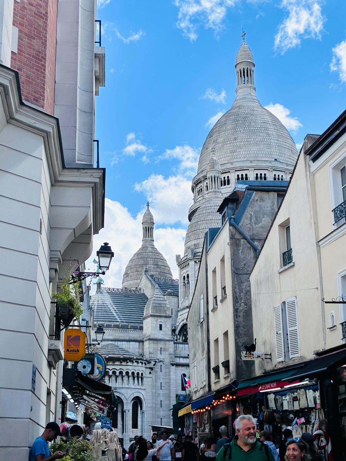 The domes of Sacré-Cœur seen past a vintage Kodak sign on a Montmartre side street.