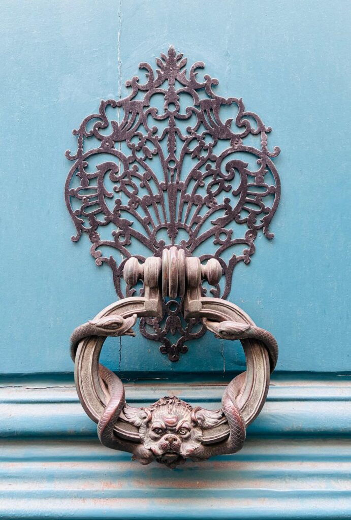 An ornate cast door knocker, two serpents framing a lion's face, on a teal-blue Paris door.