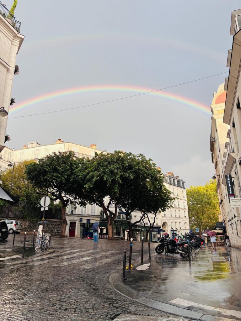 A double rainbow over a rain-wet Montmartre street, near the LCL bank and the théâtre.