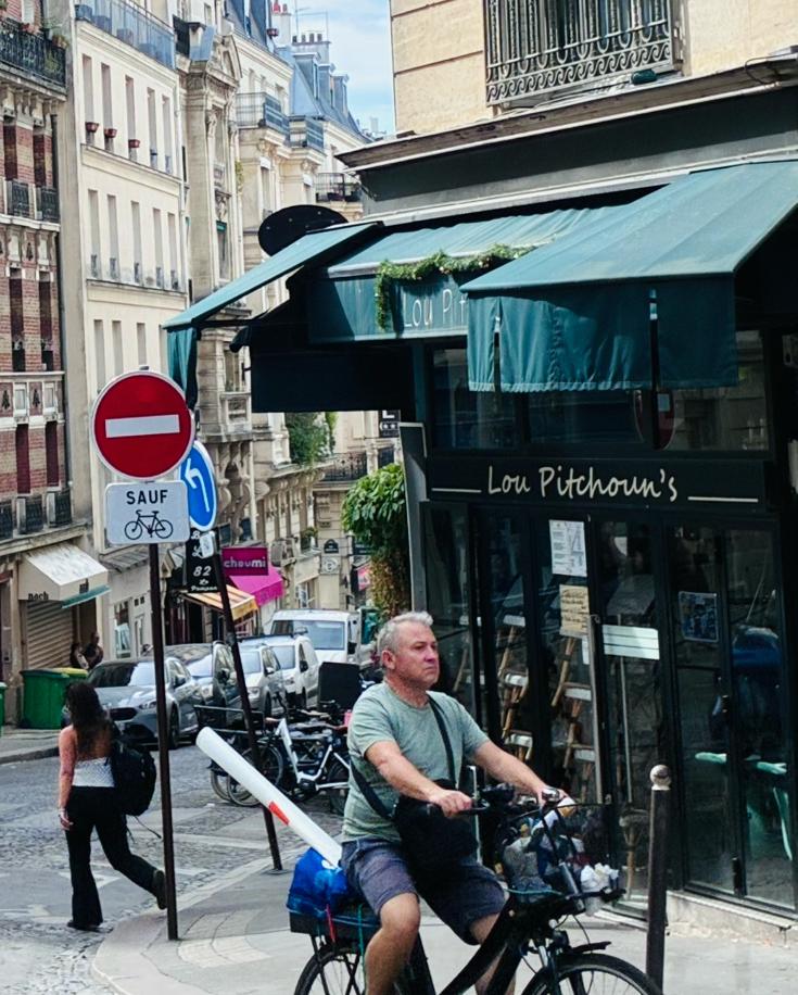 Man cycling past a no-entry sign in Montmartre, Paris, carrying a long tube under his arm