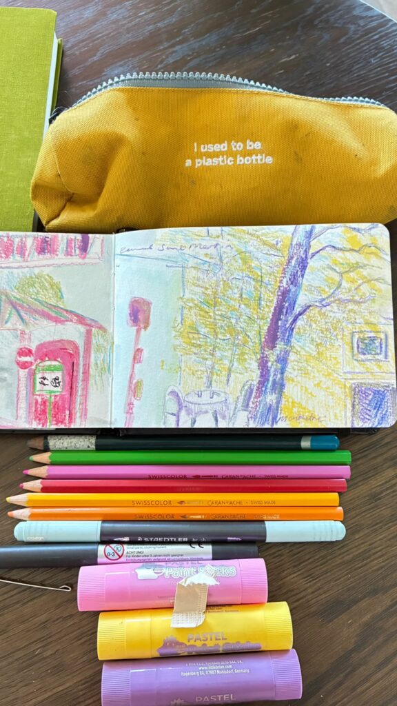 Rosie Parmley's sketchbook open to a drawing of the Canal Saint-Martin, with Caran d'Ache pencils and pastel sticks.